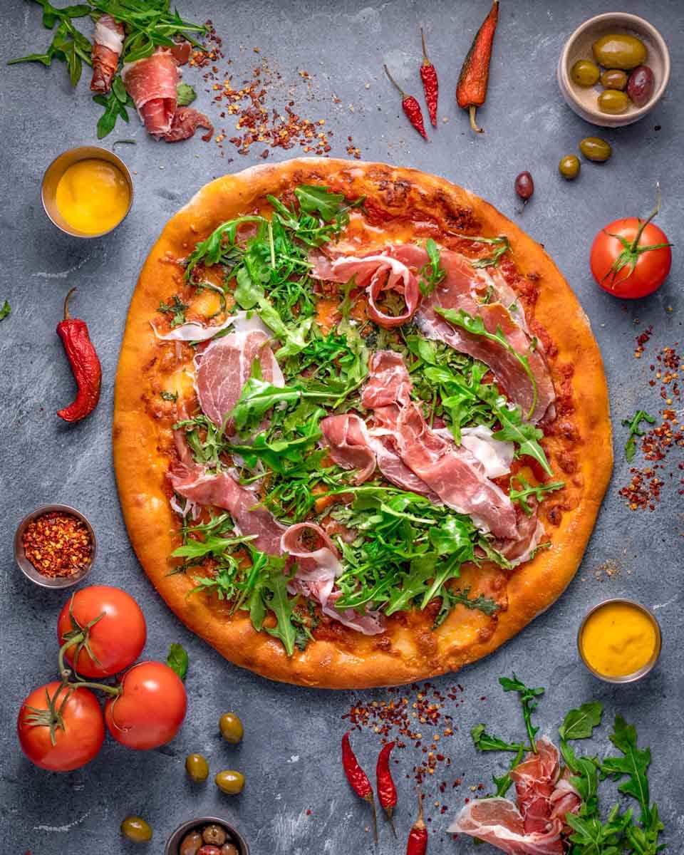 Prosciutto pizza with fresh arugula, olives, and chilli tomato base.